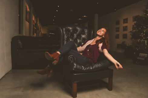 woman in maroon scoop neck shirt sitting on black leather sofa chair