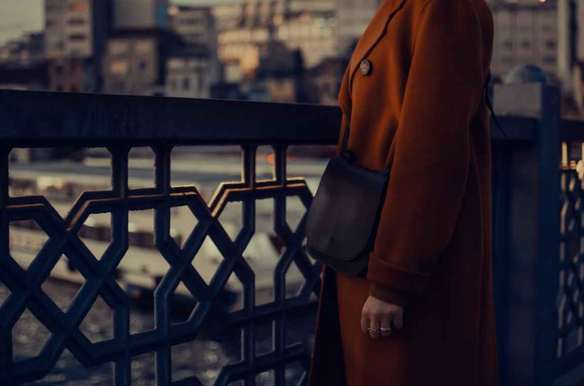 person in brown coat standing beside a metal fence of a bridge